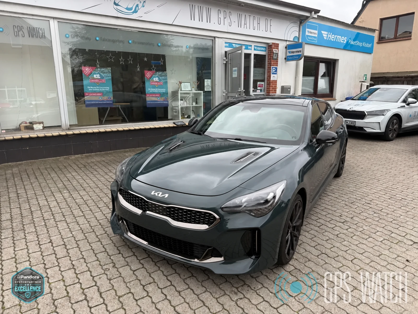 KIA Stinger vor der GPS-WATCH Werkstatt mit retuschiertem Kennzeichen und Wasserzeichen