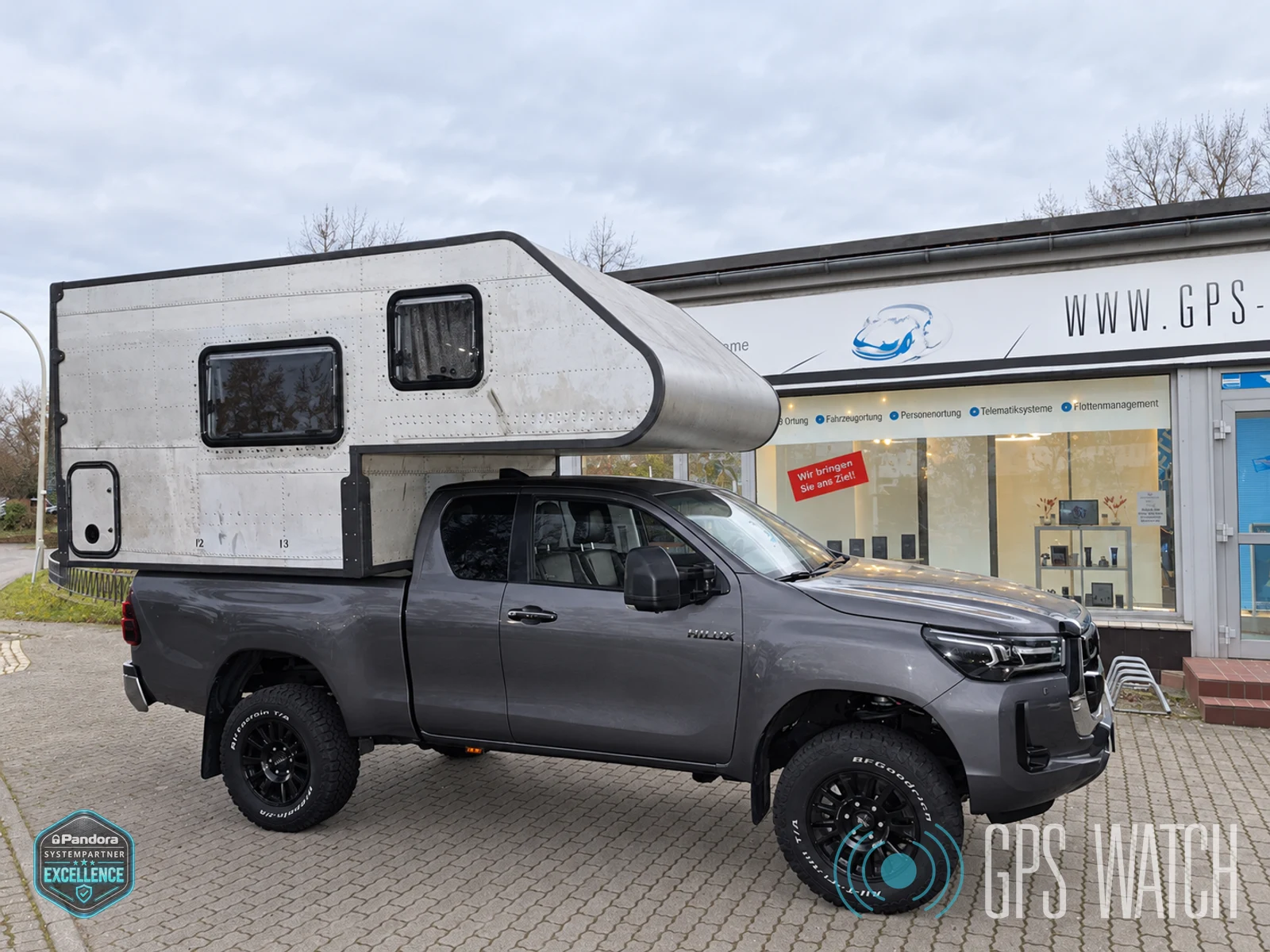 Toyota Hilux mit silberner Wohnkabine in Kisdorf, Tageslichtbearbeitung des Originalfotos mit entferntem Hintergrundfahrzeug und beiden Wasserzeichen